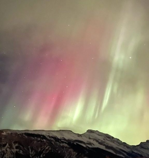 Northern Lights glowing green and pink above a mountain top